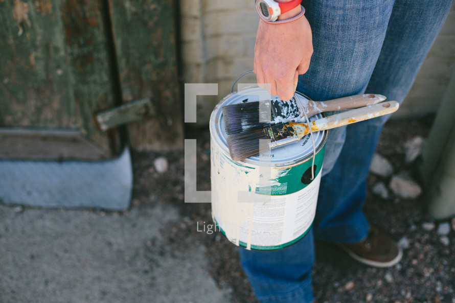 Person holding a old paint can and brushes