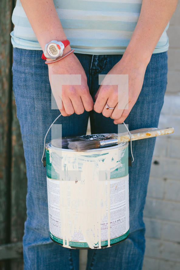woman holding a paint can and brushes out in front of her