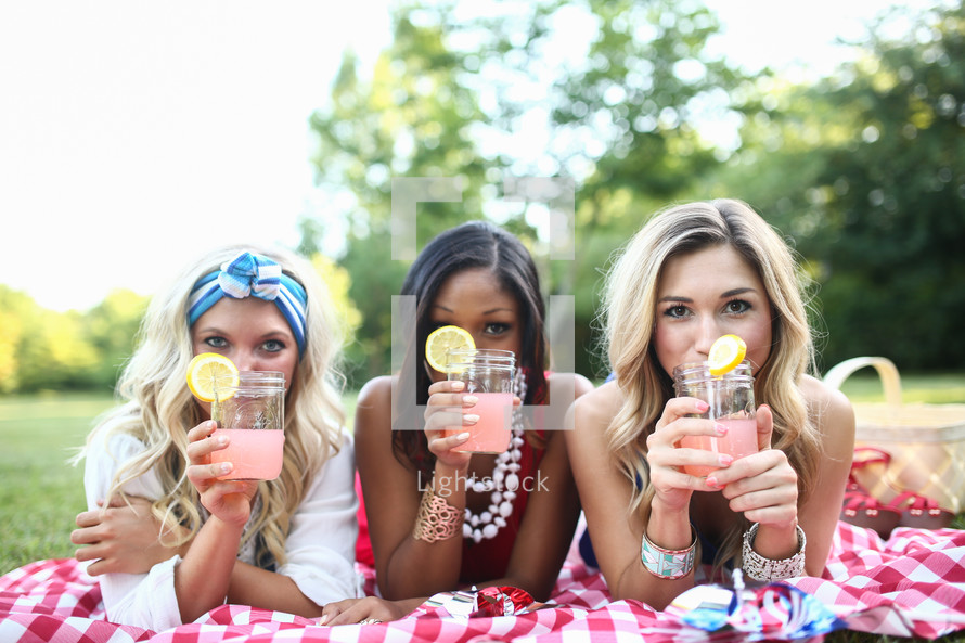 three friends drinking lemonade on a picnic blanket 