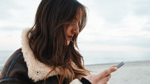 Girl chatting with a smartphone on the beach in overcast winter day