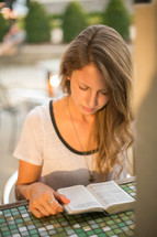 a woman reading a Bible at an outdoors table at a restaurant 