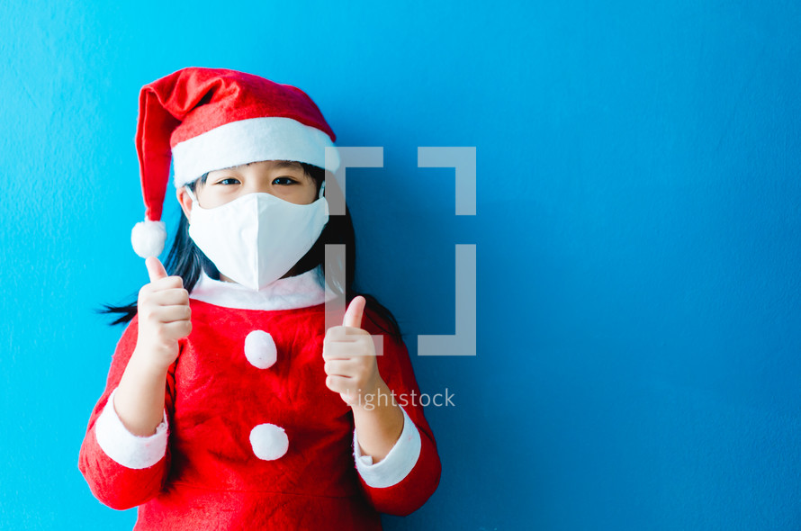 a chid in a Santa Suit putting on a face mask 