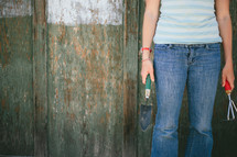 Woman holding garden tools, standing against an old wooden wall