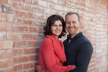Couple embracing, standing in front of a brick wall