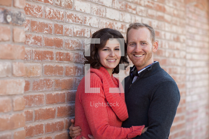 Couple embracing, standing in front of a brick wall