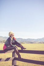 Woman sitting and balancing on a fence rail in a pasture with mountains.
