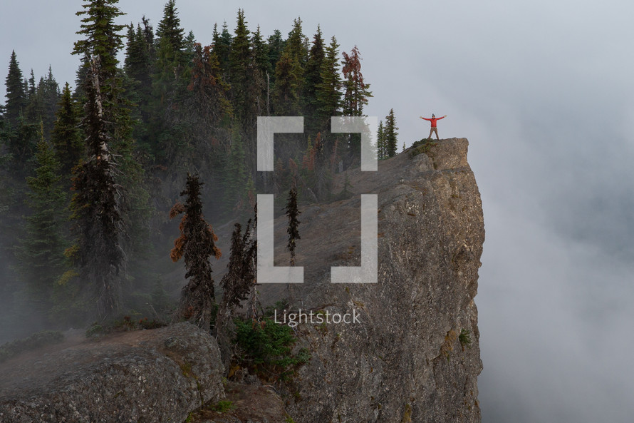 arms outstretched as a person stands on a high rock lookout 