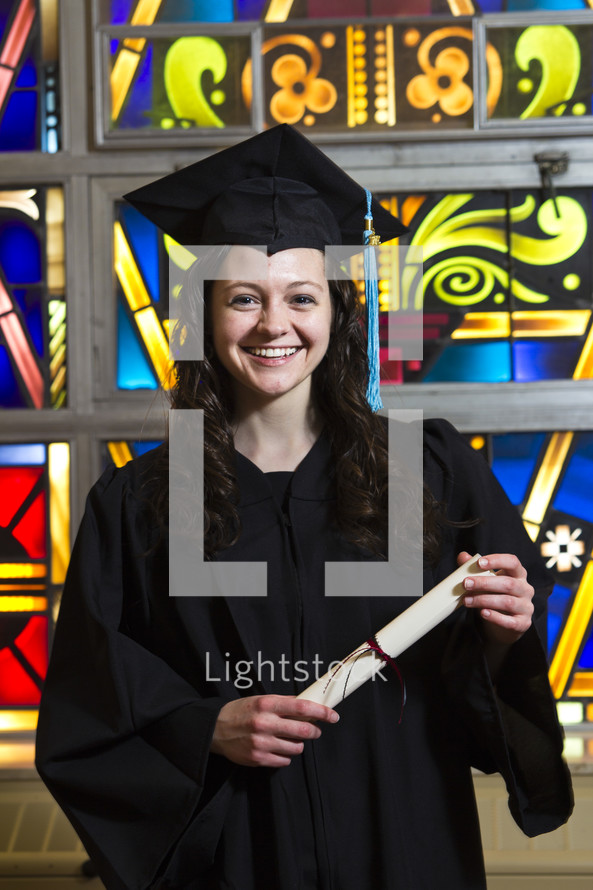 graduate holdin her diploma in front of a stained glass window