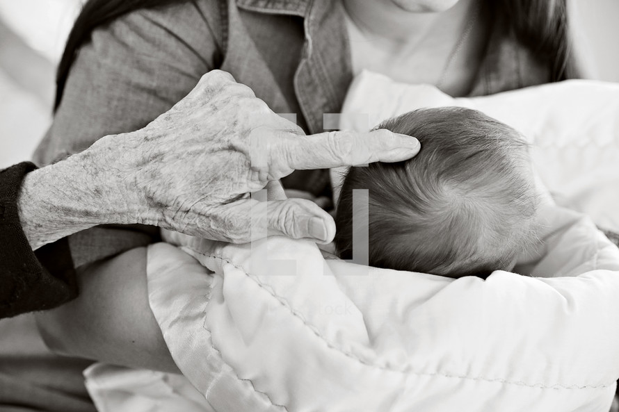 An elderly person's hand touching the head of an infant.