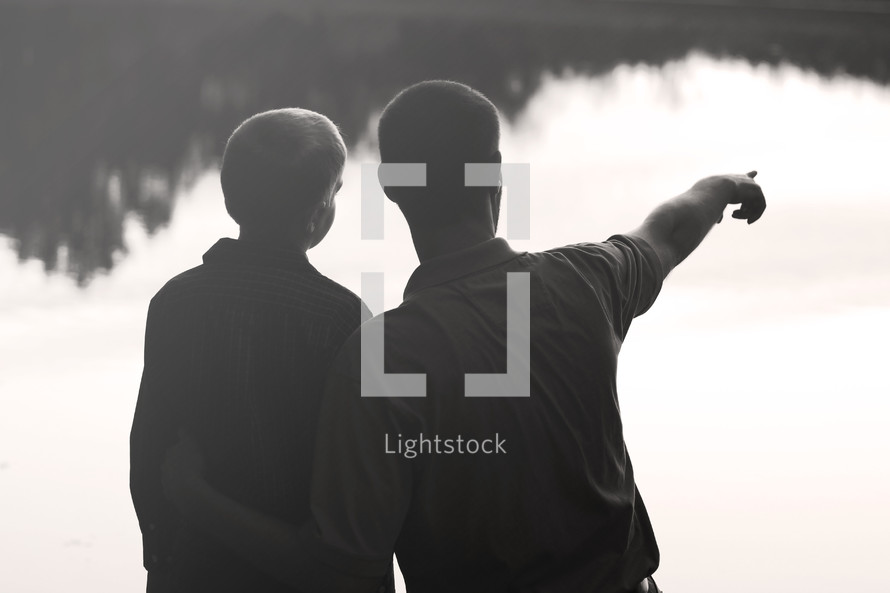 father with his son pointing at the water of a lake 