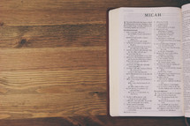 Bible on a wooden table open to the book of Micah.