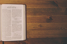 Bible on a wooden table open to the book of Matthew.