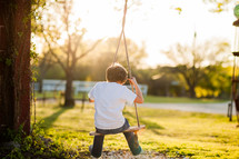Boy  young child on tree swing in the country on a farm at sunset
