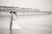 bride and groom kissing on a beach in the water