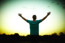 A man, with hands raised, worshipping at sunrise
