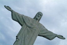 A statue of Jesus with arms extended and the sky above.
