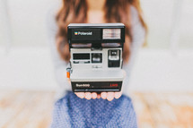 A young woman holds a Polaroid camera
