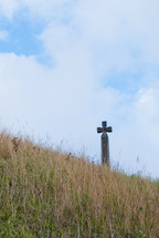 A cross in a field of grass against a blue sky.