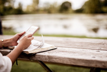woman reading a Bible outdoors and using her phone 
