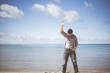 man with hand raised standing on a beach 
