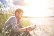 a man sitting on a beach reading a Bible 