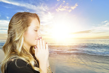 woman with praying hands on a beach 