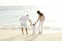 A young family stands on the beach at the edge of the ocean.  
