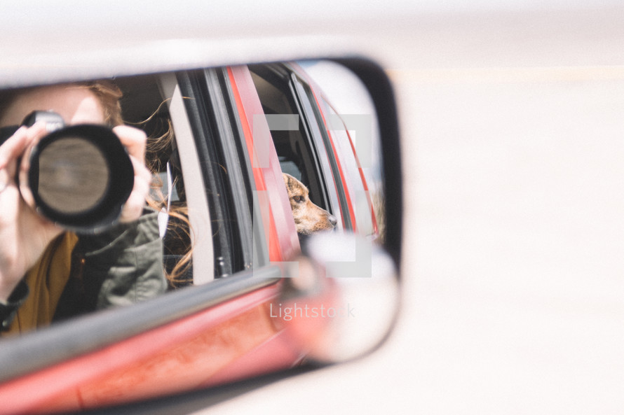 woman in a rearview mirror taking a picture with a camera 