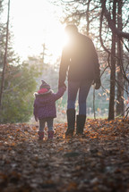 mother and toddler daughter walking holding hands in a forest 