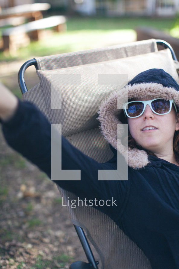 a woman in a hoodie lying in a lounge chair 