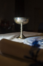 Silver chalice sitting on top of table with tablecloth.