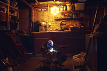 Basement workshop filled with tools, laundray basket, and an antique baby strioller lit with one lightbulb.