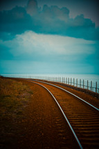 A train track curving along an ocean shore.