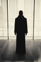 dark silhouette - priestly figure standing - window