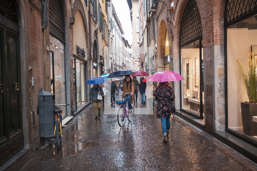 People walking on a cobblestone street in Greece in the rain 