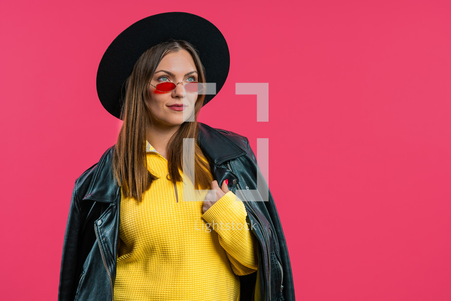 Pretty stylish woman on pink background. Smiling lady in hat and sunglasses with european appearance looking at camera. High quality photo
