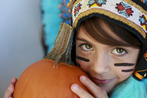 A child in a costume, holding a pumpkin.