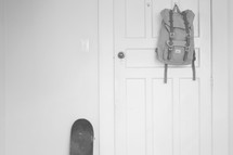 a book bag hanging on a door and a skateboard 