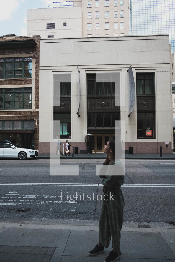 a woman standing on a downtown sidewalk looking up 