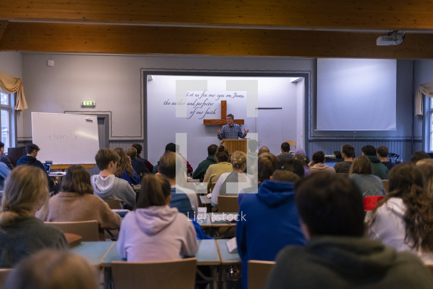 People sitting at tables in a chapel, classroom while someone teaches from the front