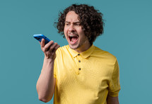 Annoyed young man quarreling while talking on mobile phone. Angry dude, stress. Blue studio background. Conflict, dispute, negative. High quality