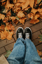 Female feet in sneakers with yellow fallen maple leaves. Autumn background. High quality photo