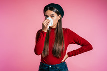 Young girl with long hair sneezes into tissue. Isolated woman is sick, has a cold or has allergic reaction. Health, medicine, illness, treatment concept