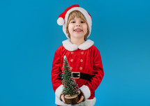 Friendly little Christmas boy in Santa Claus costume on blue background. Happy emotional child with artificial beard. High quality photo