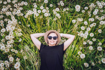 Young beautiful girl in sunglasses lies in dandelion field and looks to the sky. Top view