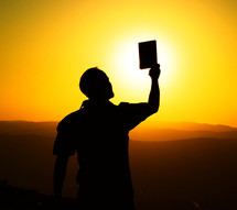 silhouette of a man holding up a Bible 