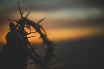 silhouette of a man holding up a crown of thorns  at sunset 