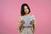 Satisfied woman in floral dress holding files papers isolated on pink background. Pretty girl checks documents, utility bills