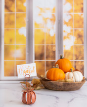 Orange and white pumpkins with a thankful sign in front of autumn window