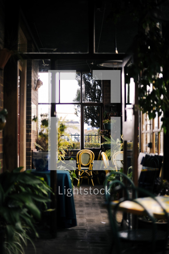 Empty chairs and tables in a quiet café, lit by beautiful, big, old glass windows. Vintage feel to the colour in this image.